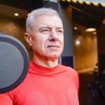 Elderly man in a gym wearing a red shirt, lifting a dumbbell, showcasing active lifestyle.